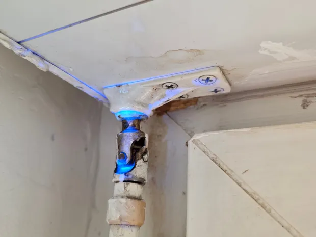 Fuite localisée à la lumière UV bleue sur un raccord de tuyauterie au plafond, mise en évidence lors d'une intervention de GBL Détection.