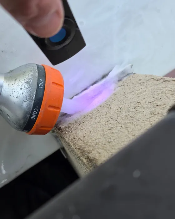 Technicien de GBL Détection utilisant une lampe UV pour révéler un colorant fluorescent violet sur un acrotère de toiture-terrasse.