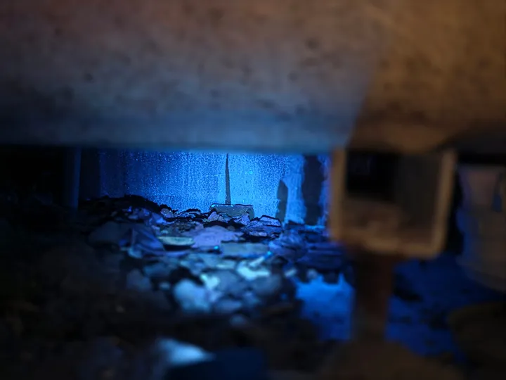 Aiguille de traçage plantée dans un vide sanitaire éclairé en lumière UV bleue lors d'une recherche de fuite par GBL Détection.