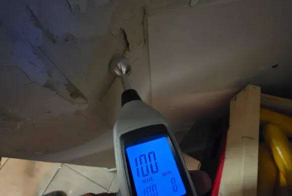 Humidimètre sans contact affichant 100 % de saturation sur un plafond décollé et taché d'humidité, diagnostic de fuite par GBL Détection.